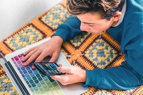 Sind Lootboxen Glücksspiel? Teenager tippt auf Laptop und Smartphone gleichzeitig