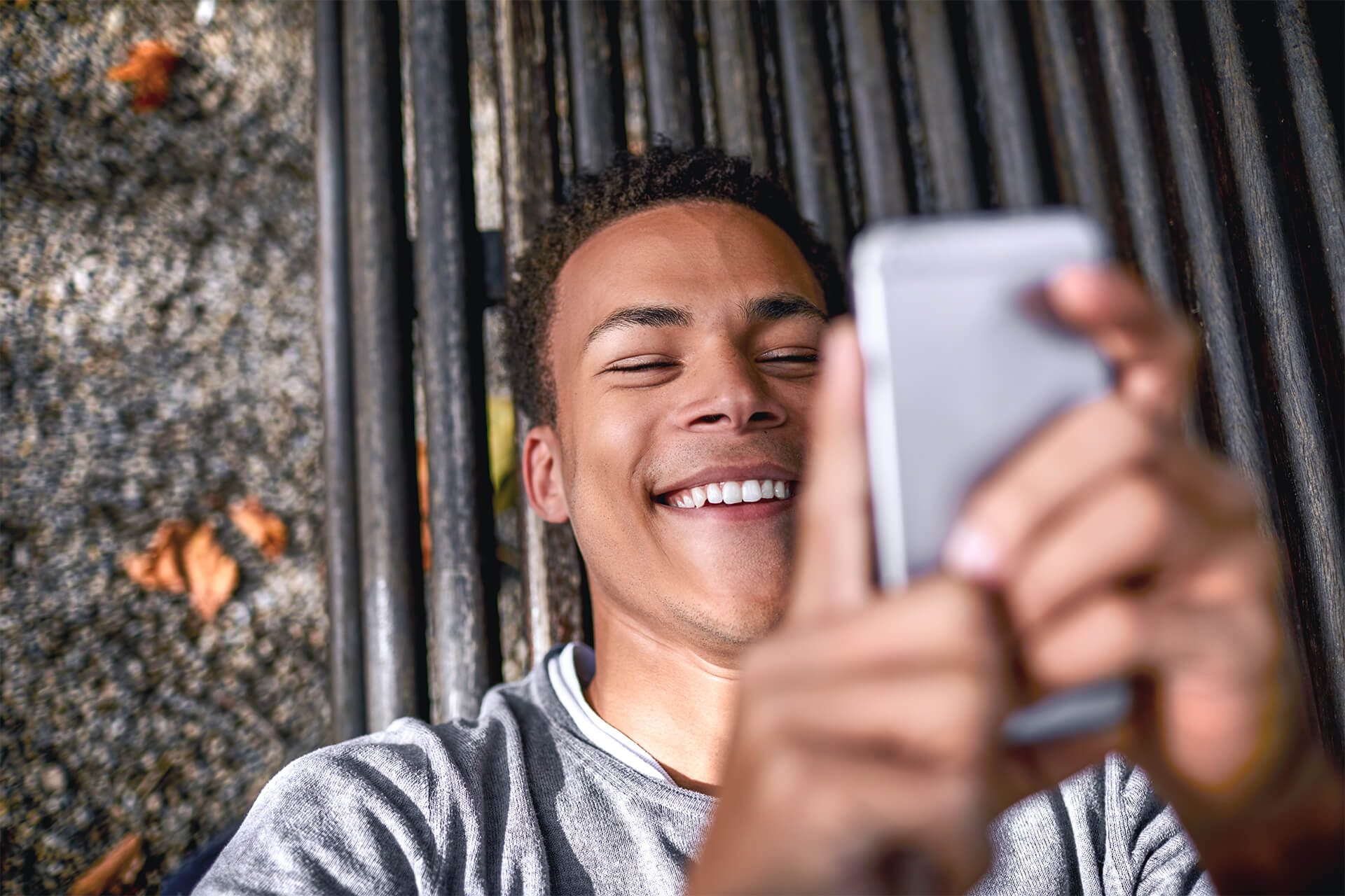 Jugendlicher liegt auf einer Bank und schaut in sein Smartphone.
